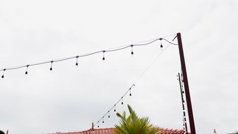outdoor string lights suspended across cloudy sky with palm and tiled roof