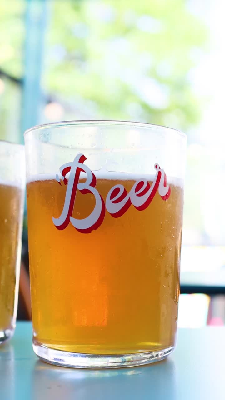 Un singolo bicchiere di birra dorata è posato su un tavolo con uno sfondo sfocato.