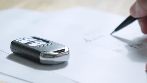 man signs documents with focus on cars key