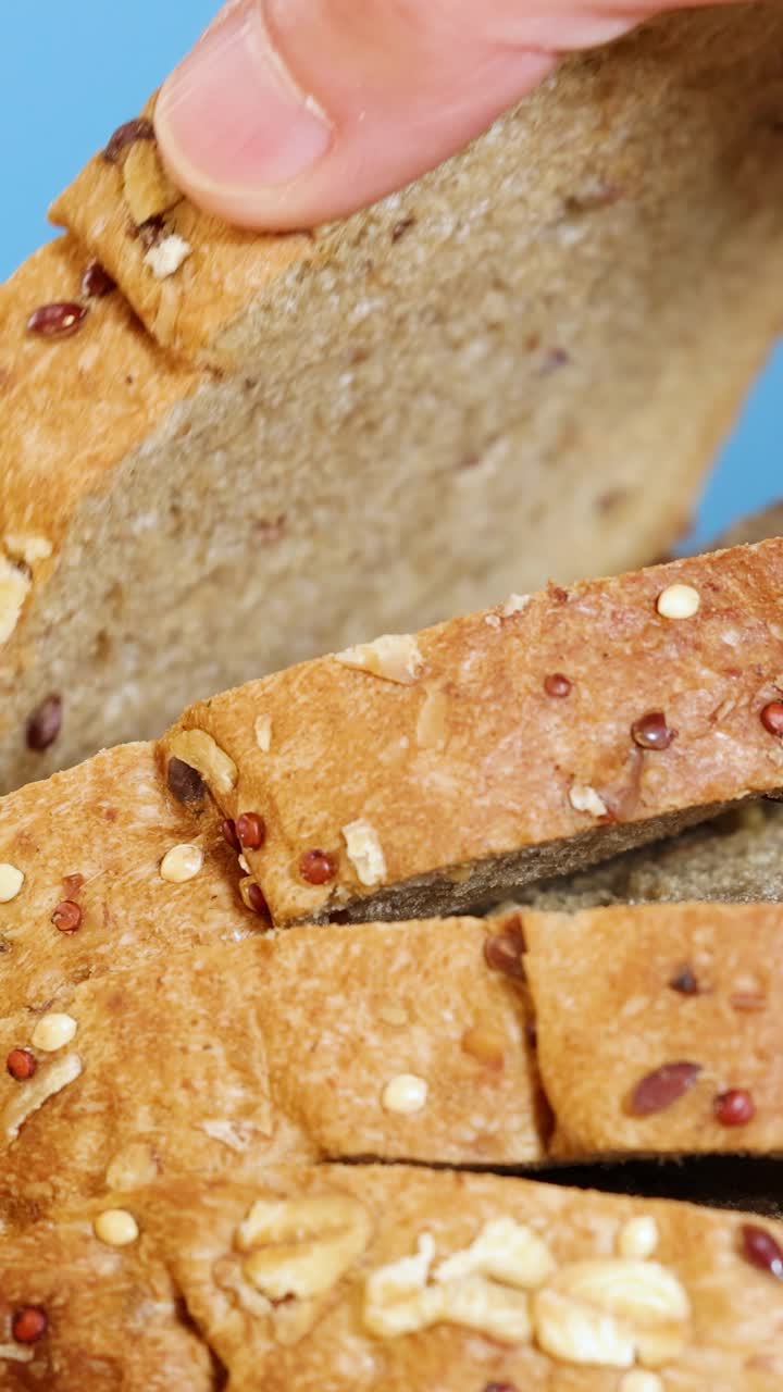 A hand removes a slice from a seeded whole wheat bread loaf against a blue background
