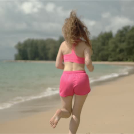mujer activa en ropa deportiva rosa corriendo en la playa