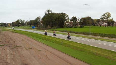 three motorbikes in flat, green grass, dutch landscape, riding on pavement