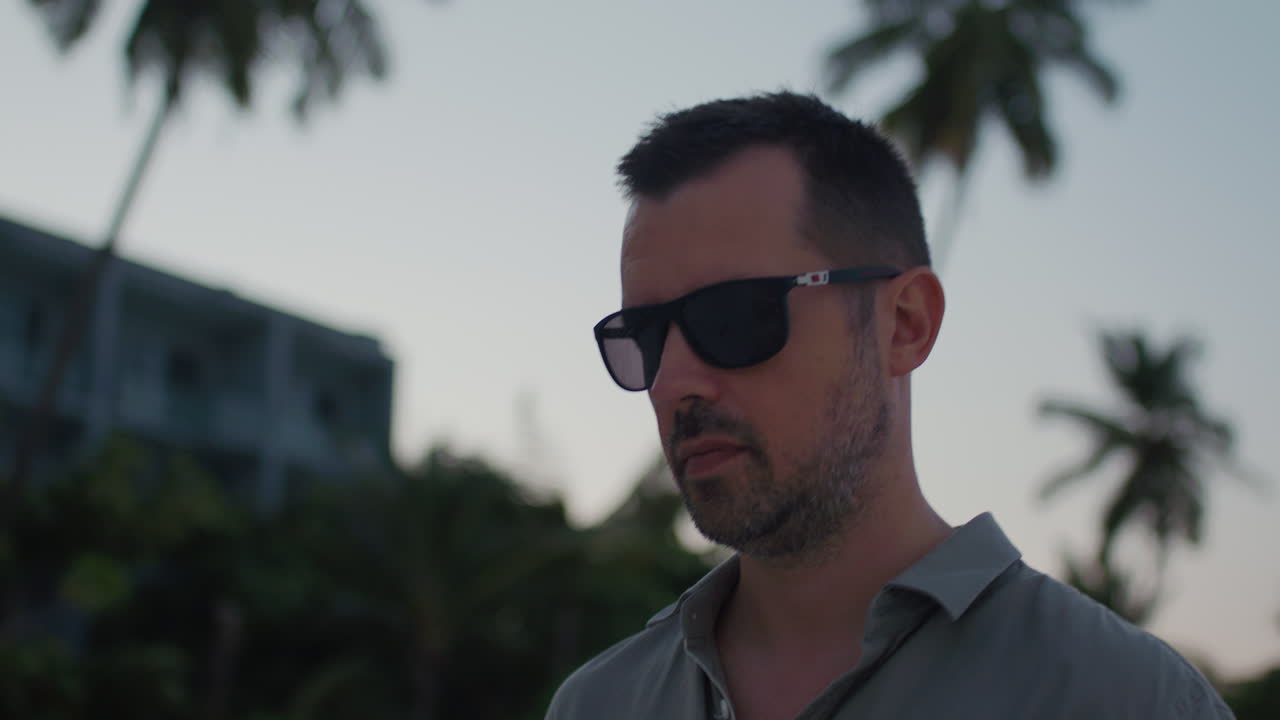 Close up on cool and confident man in cool sun glasses walk along tropical beach on the sunset.