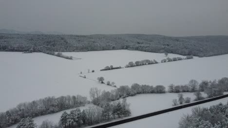 Drone-flies-over-winter-landscape-with-mountains-and-fields