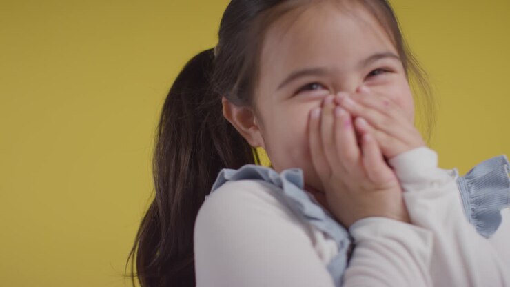 Studio Portrait Of Shy Young Girl Smiling And Laughing Against Yellow Background 2