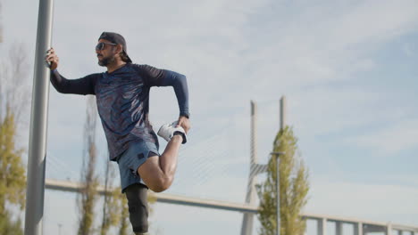 focused sportsman with artificial leg warming up and stretching leg before outdoor workout