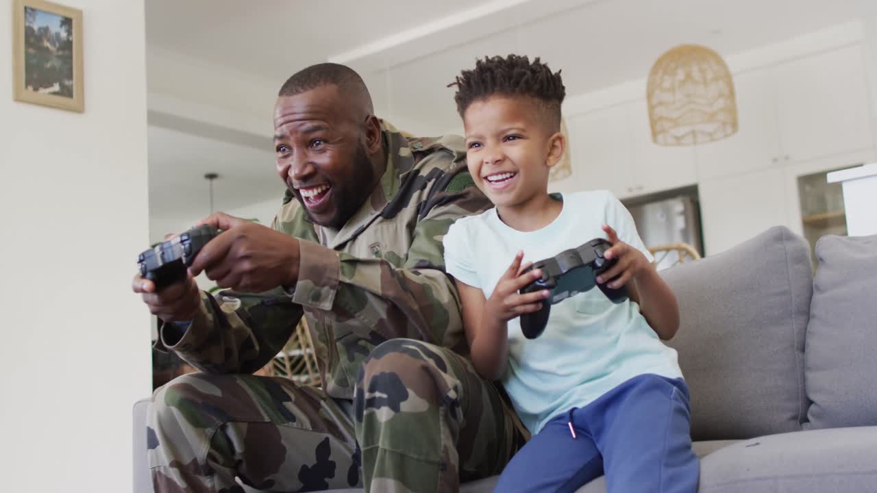 feliz padre afroamericano y su hijo sentados en el sofá y jugando videojuegos