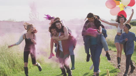 grupo de jóvenes amigos emocionados caminando por el sitio del festival de música llevando bengalas y globos