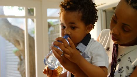 side view of young black mother feeding water to her son in kitchen of comfortable home 4k