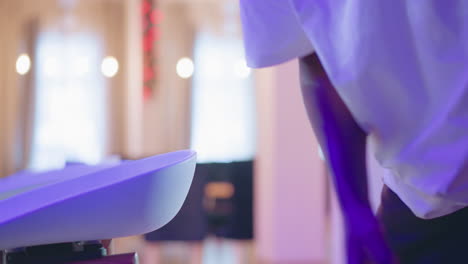 close-up of a person s hand adjusting bar stools in a modern lounge with purple lighting, festive decor, and stylish seating. a scene of hospitality staff setting up the bar area for service