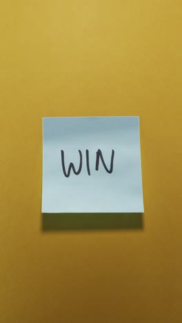hands posting win sticky note on yellow wall, showcasing success
