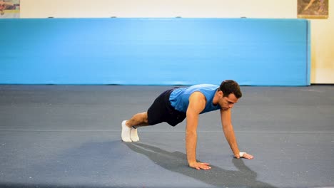 a guy doing a special kind of push up in a top-side-front view still shot inside a gymnastics gym