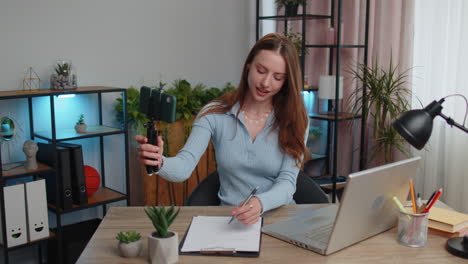 Young-business-woman-blogger-using-smartphone-shooting-video-call-for-social-media-at-home-office