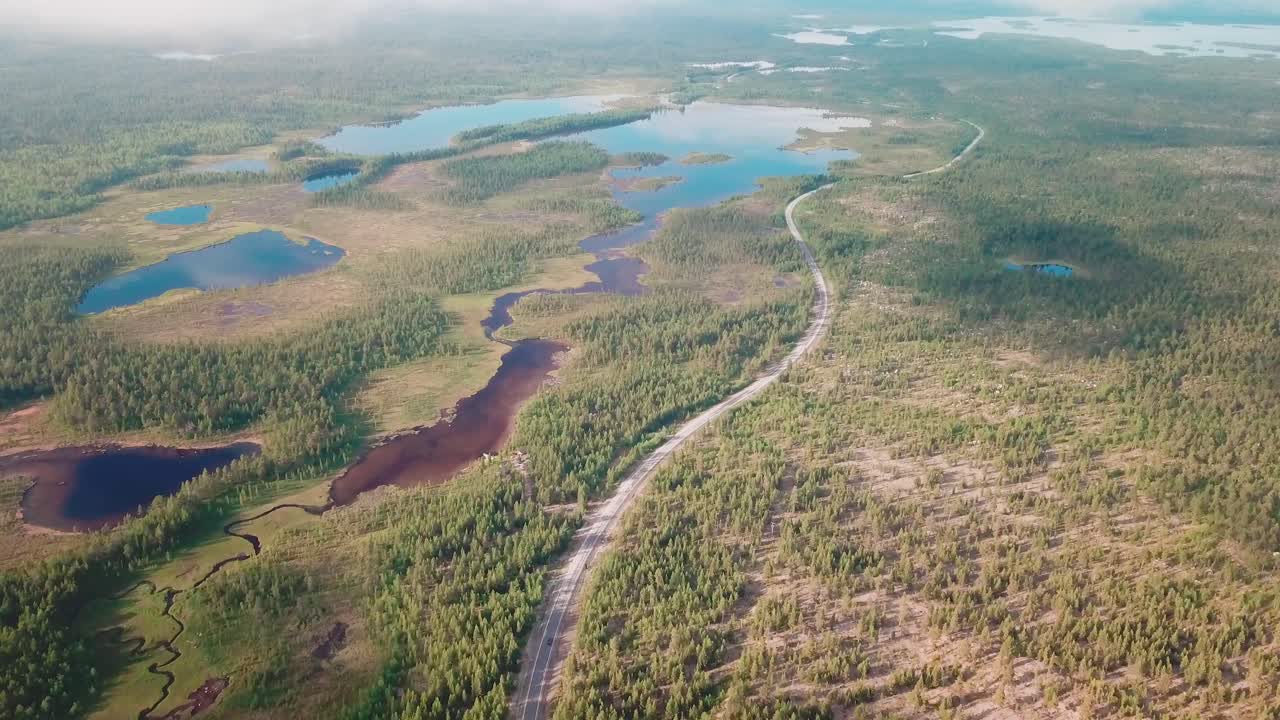 Ujęcie dronem w przód nad dużym parkiem narodowym z krętą drogą i samochodem w północnej Finlandii.