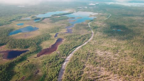 Forward-drone-shot-over-a-large-national-park-with-a-winding-road-and-a-car-north-of-Finland