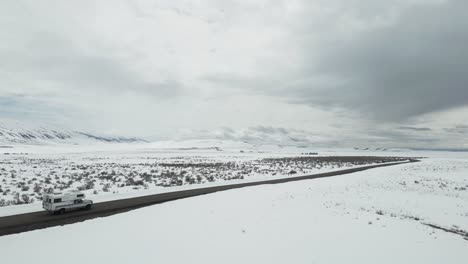 Vista-Aérea-De-Una-Autocaravana-Blanca-Que-Recorre-El-Paisaje-árido-Y-Nevado-De-Idaho.