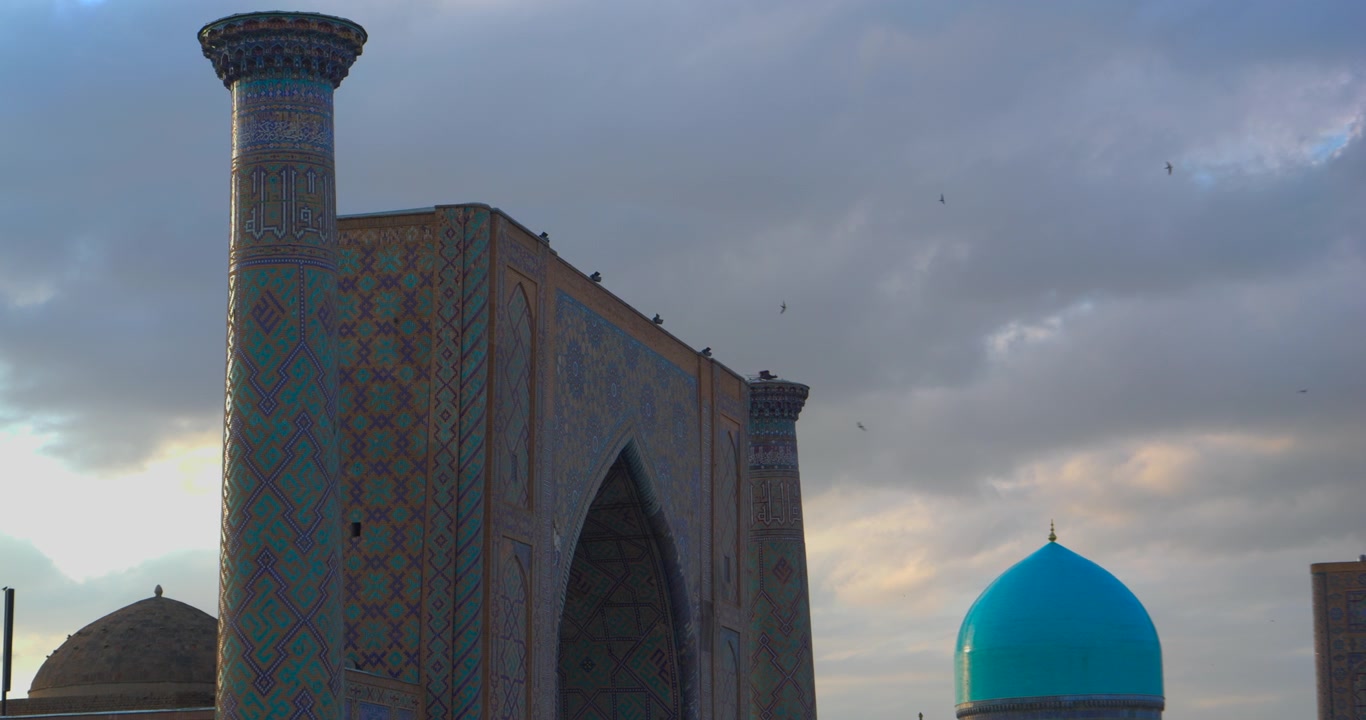 Close view of Registan minaret tiled portal and turquoise dome under dramatic cloudy sky in Samarkand Uzbekistan Central Asian Islamic architecture travel heritage and historic landmark concept