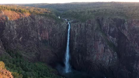 wallaman falls in queensland dusk aerial view moving backwards, tall waterfall with golden sunlight