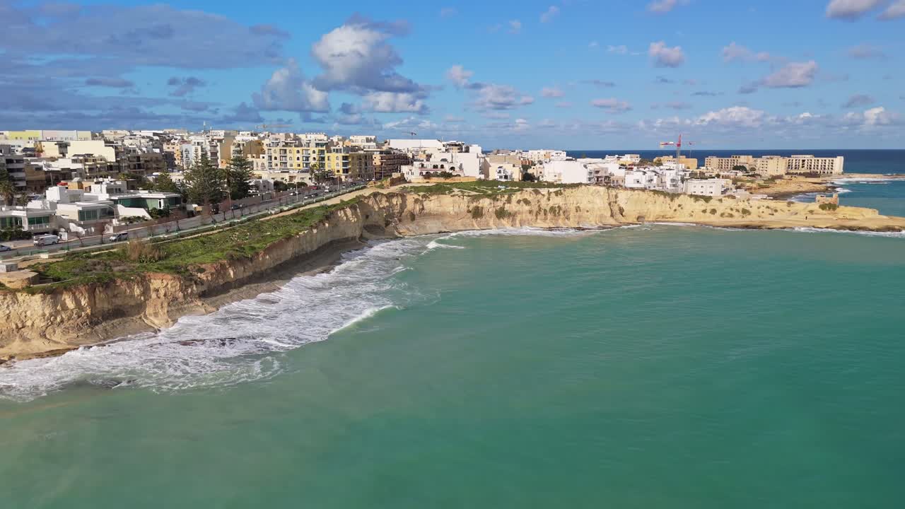Mare turbolento e ondoso che bagna le scogliere calcaree di St Thomas Bay, il giorno dopo il passaggio della tempesta Harry, con gli edifici costieri di Marsaskala sullo sfondo in una soleggiata giornata invernale a Malta