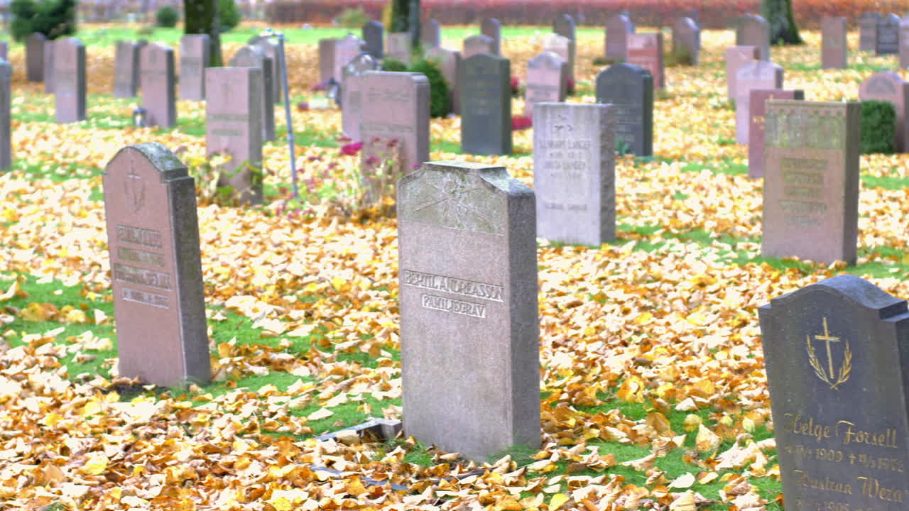Many graves with autumn leaves lying on the ground in Kviberg Cemetery in Gothenburg, Sweden - pan over