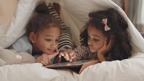 sisters using tablet computer under blanket