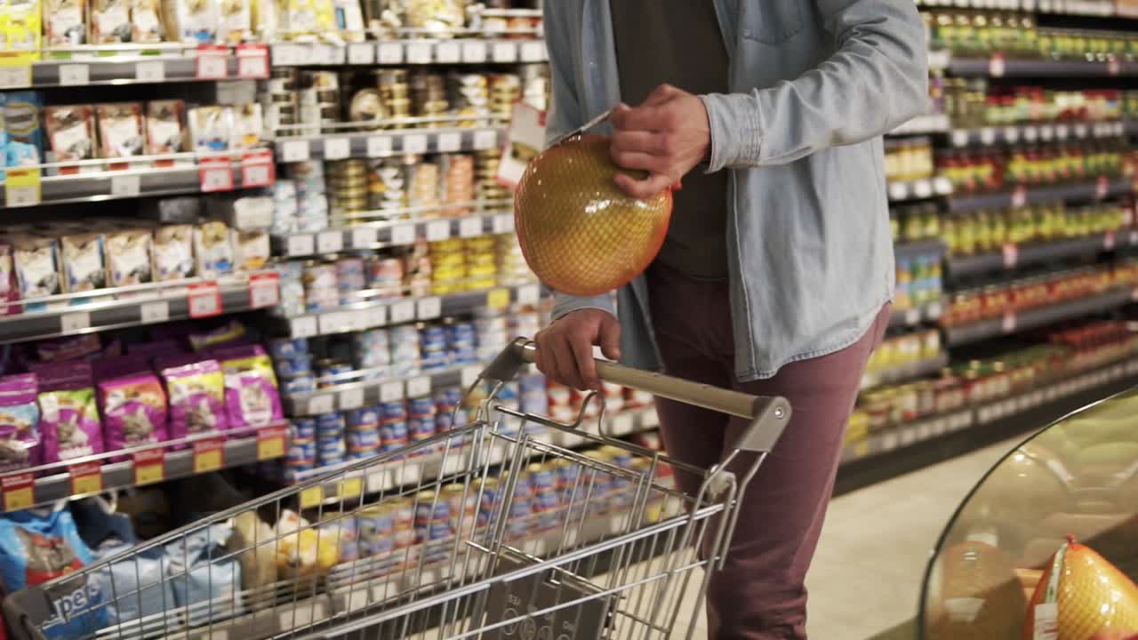 imágenes recortadas de un hombre irreconocible con camisa azul comprando frutas y verduras en el departamento de productos de un supermercado de una tienda de comestibles. tomando fruta de pomelo, poniéndola en el carrito de compras y caminando más. grandes estantes de comestibles en el fondo
