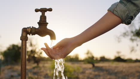 Frau-Wäscht-Sich-Bei-Sonnenaufgang-Auf-Ländlichem-Ackerland-Die-Hände-Unter-Leitungswasser-Mit-Frischem-Wasser