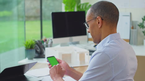 Rückansicht-Eines-Reifen-Männlichen-Architekten,-Der-Im-Büro-Am-Schreibtisch-Am-Laptop-Arbeitet-Und-Auf-Dem-Mobiltelefon-Surft