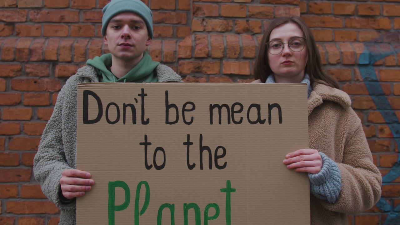 крупным планом молодые мужчина и женщина активисты смотрят в камеру, держа картонный плакат во время акции протеста против изменения климата