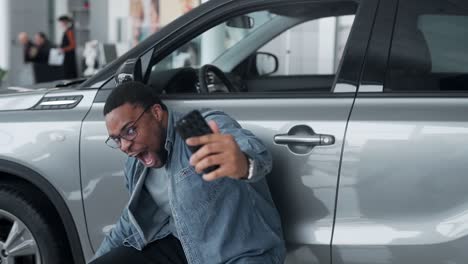 a black man happily shoots a video near the car in a car dealership