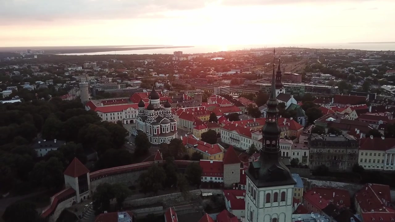 Filmato mozzafiato con drone del Centro Storico medievale di Tallinn al tramonto. L'inquadratura mostra la Collina di Toompea, la Cattedrale di Santa Maria e gli edifici dai tetti rossi sotto un cielo drammatico di nuvole rosa e arancioni.