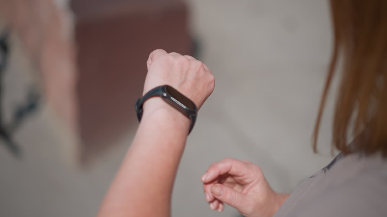 Close up of woman tapping smartwatch under bright sun with blurred background, gesture showing connection with technology, awareness of time, and focus on modern routine