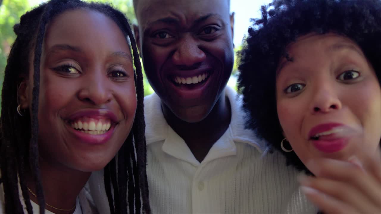 African American friends posing for selfie, left woman holding phone, leaning in laughing near pool