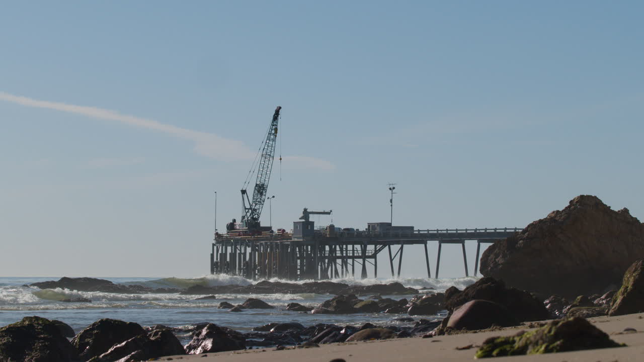 muelle de perforación de plataformas petrolíferas con olas rompiendo en una playa rocosa con grúa a cámara lenta 4k 60fps