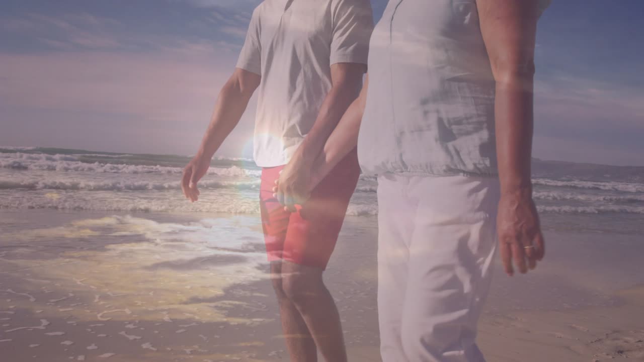 Coppia matura che cammina sulla spiaggia, con l'inquadratura della telecamera che causa bagliori dell'obiettivo rivelando un anello e i piedi, per il viaggio.