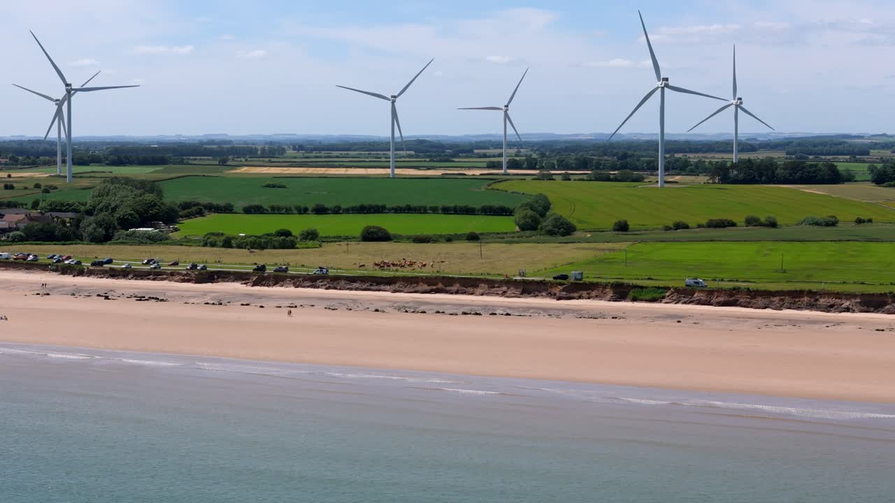Drone Aerial footage of a wind turbine, windmill turning in the wind on a wind farm close to a beach in the North of England showing renewable energy efficient wind power.