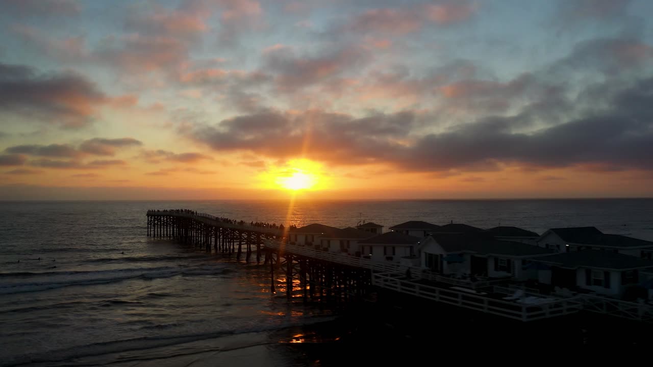 Drone naik ke kiri di atas Dermaga Crystal di Pacific Beach San Diego saat matahari terbenam dengan sinar matahari memantul dari laut