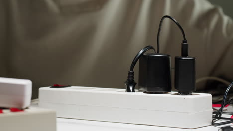 white power strip with many various of cords and cables in close-up. an extension cord with many power sockets. adapter with phone, headphones, usb connectors.tangled wires on table. trying to untangle many messy cables.