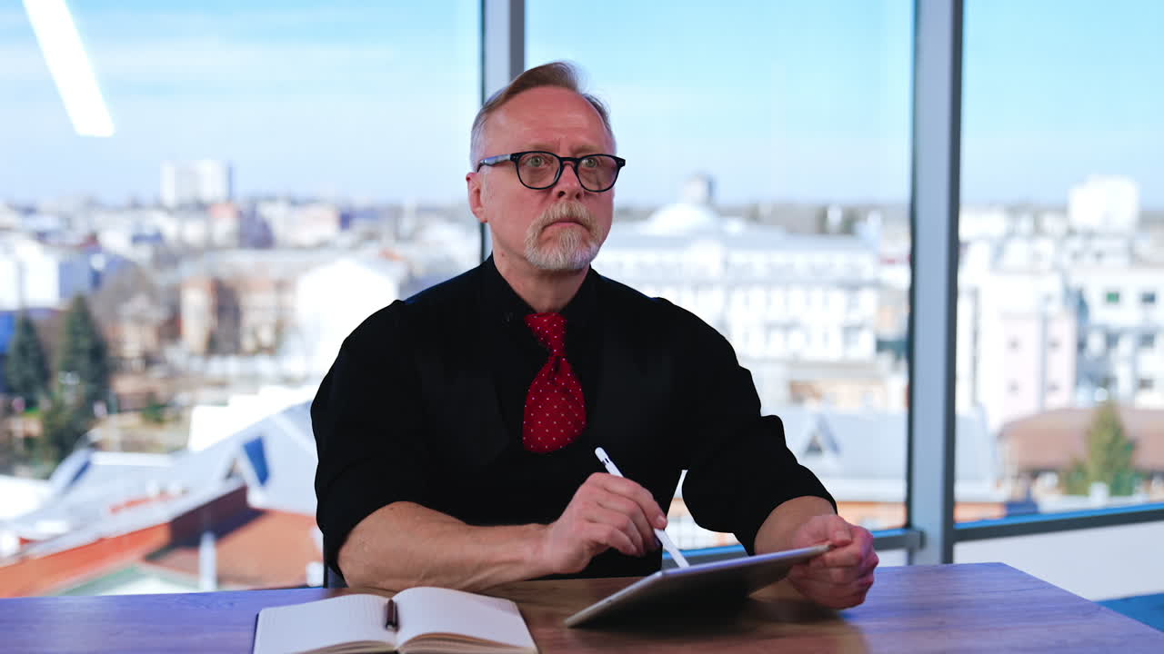 Serious Caucasian entrepreneur works with I-pad. Businessman in the office with panoramic window. Blurred backdrop.