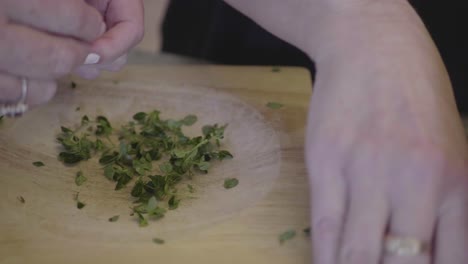 closeup of a woman chopping thym herb on a wooden board in the kitchen