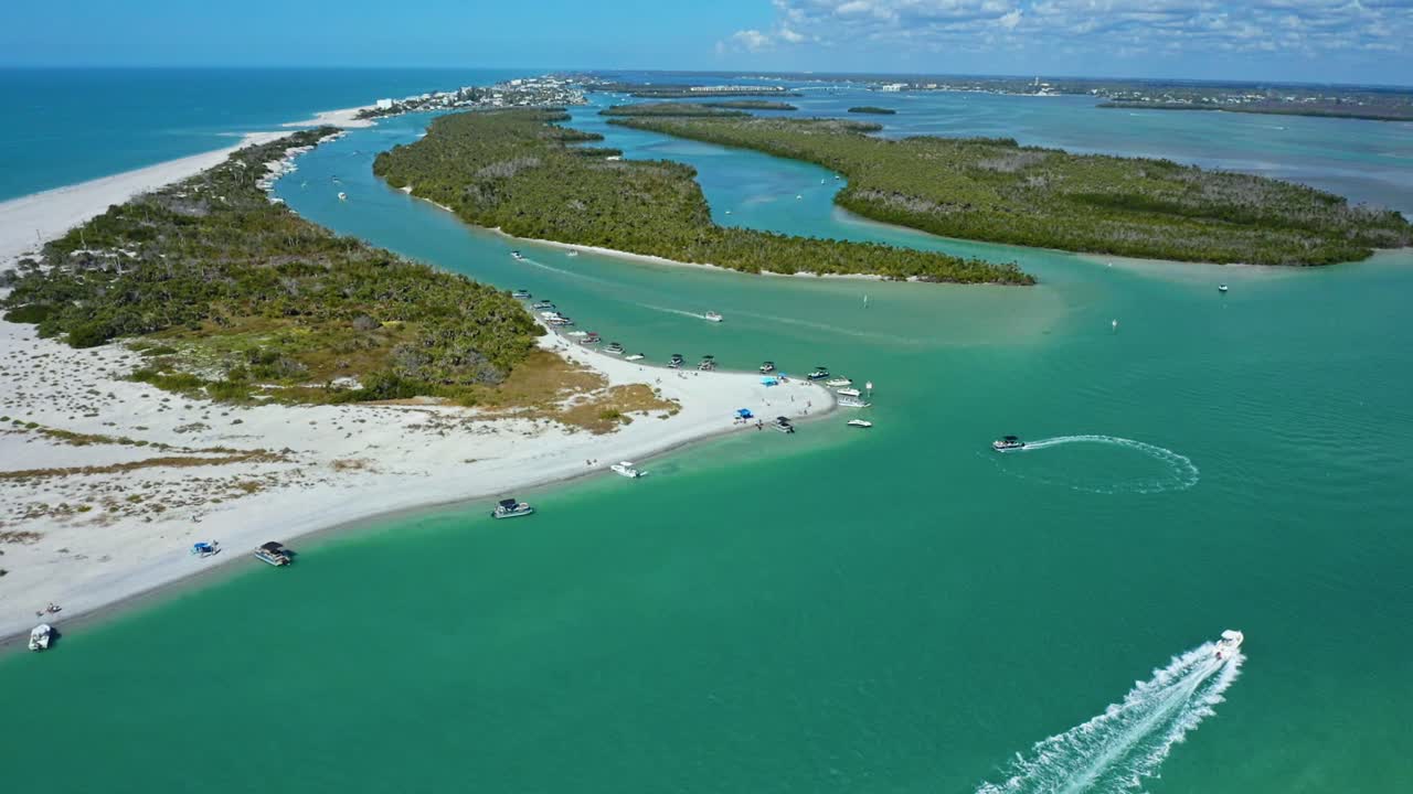 Un'insenatura costiera delimitata da spiagge sabbiose e isole di mangrovie mostra diverse barche che navigano e sono ancorate in acque cristalline turchesi sotto un cielo parzialmente nuvoloso.