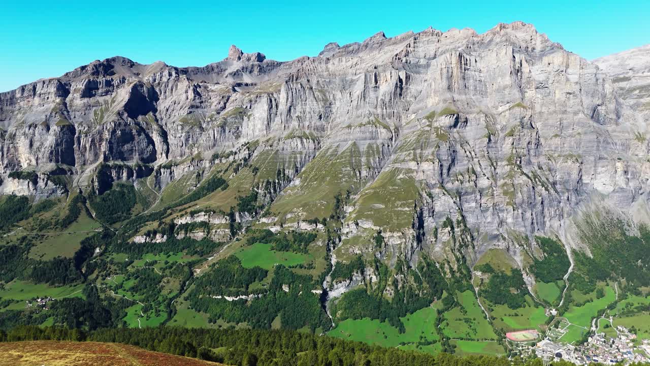 Wide view of the impressive rocky mountains and green valleys near Leukerbad, Switzerland. Scenic alpine landscape under clear blue sky, perfect for travel, tourism, and nature concepts
