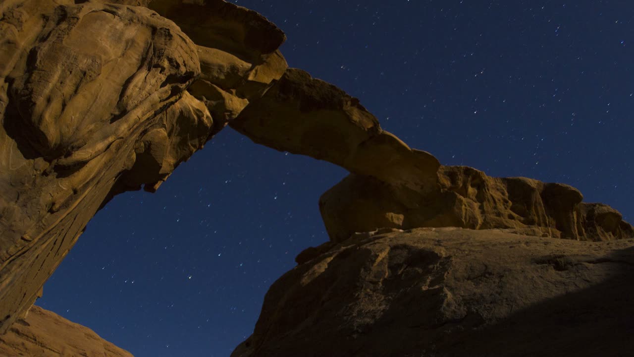 un increíble lapso de tiempo mirando una formación de arco en el desierto contra un cielo nocturno