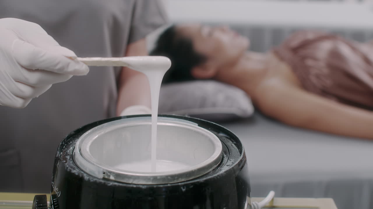 Hand of Beautician Heating Wax for Depilation Procedure