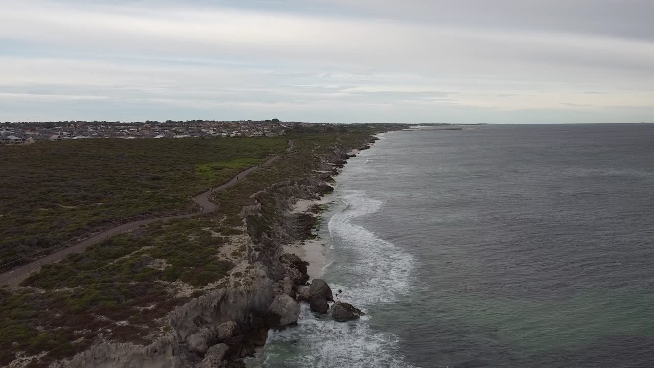 Vagues s'écrasant sur le littoral rocheux, vue aérienne avec des promeneurs sur le sentier