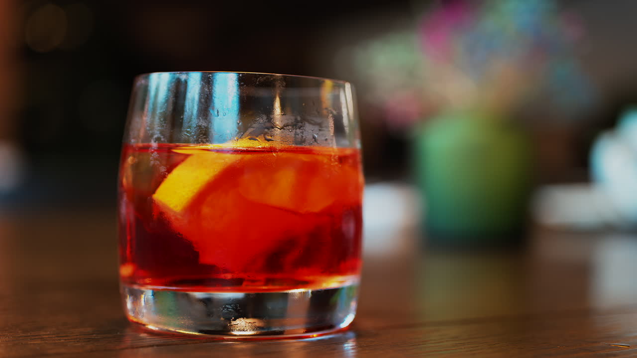 Close up of a Negroni cocktail with orange slice and ice cubes on a wooden table