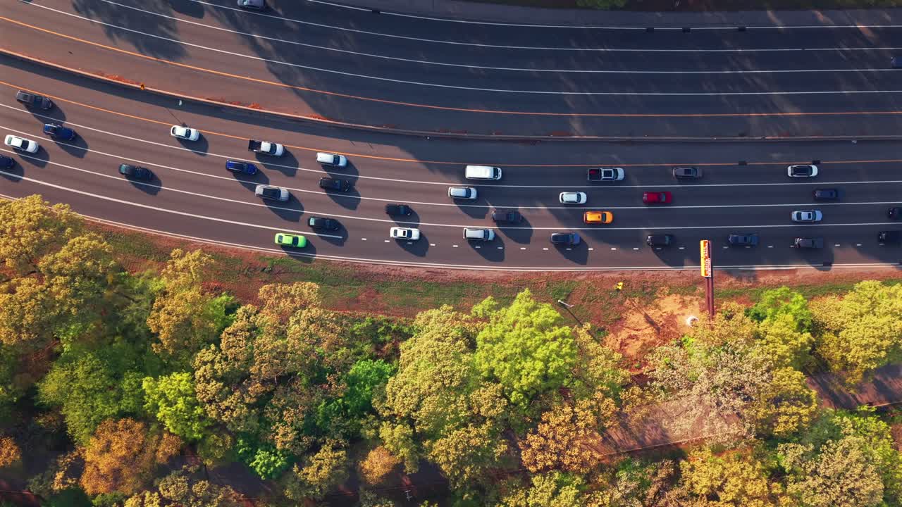 An aerial top down view by the Southern State Parkway on Long Island, NY, taken during a bright and sunny day. The drone hovers right beside the parkway, looking down from high above green treetops.