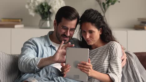 Young married couple relaxing on sofa using tablet device