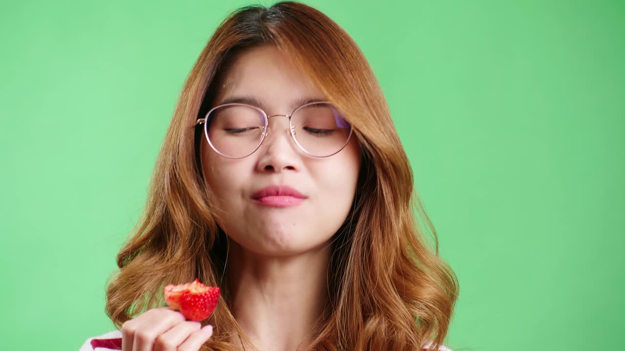 Young woman enjoying strawberry in the studio with green screen chroma key background