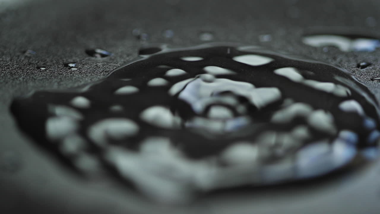 захват капли воды в замедленной съемке на макрокамеру с близкого расстояния, когда она ударяется о водопроводную гладину и помалу на темном фоне тарелки со светлым отражением